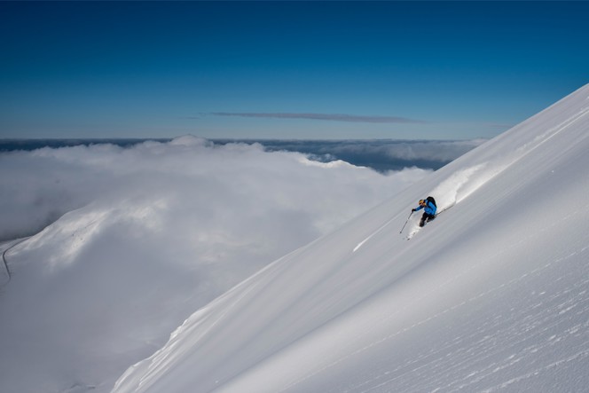 A skier headed down a mountain above the clouds on a clear day.